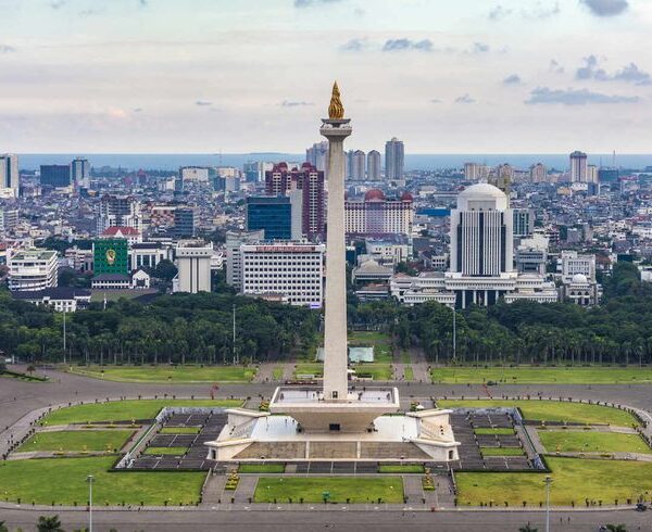 National Monument (Monas) in Jakarta, Indonesia, standing tall among the modern city skyline with skyscrapers and the golden flame monument visible during sunset.