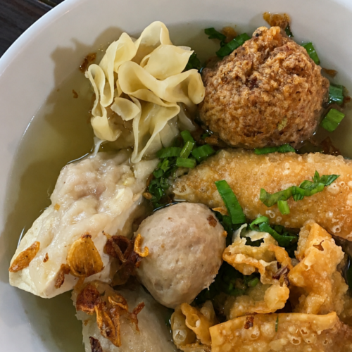 A bowl of Bakso Malang featuring meatballs, fried dumplings, tofu, siomay, crispy wontons, and clear savory broth served at Bakso Malang restaurant in Indonesia.