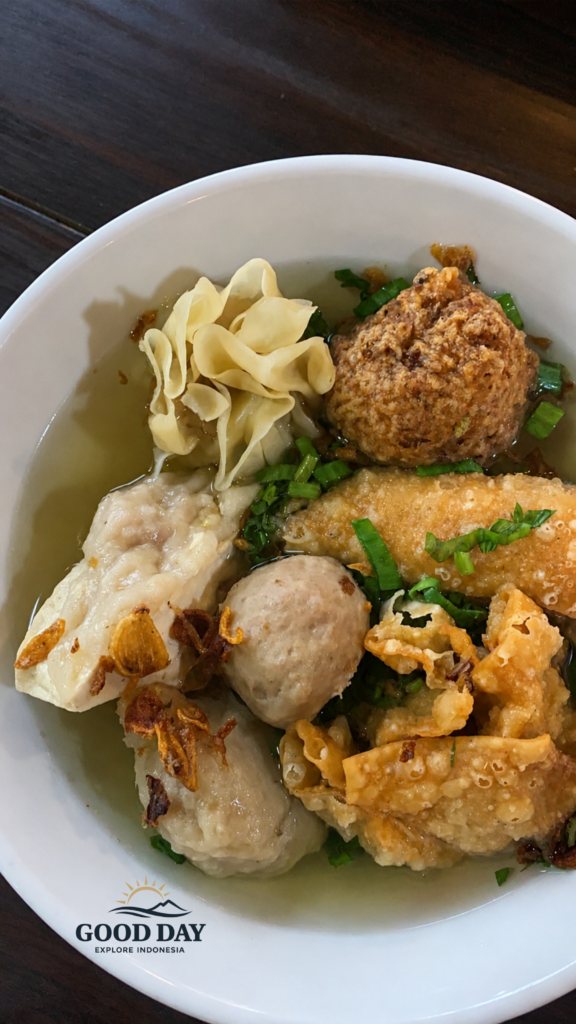 A bowl of Bakso Malang featuring meatballs, fried dumplings, tofu, siomay, crispy wontons, and clear savory broth served at Bakso Malang restaurant in Indonesia.