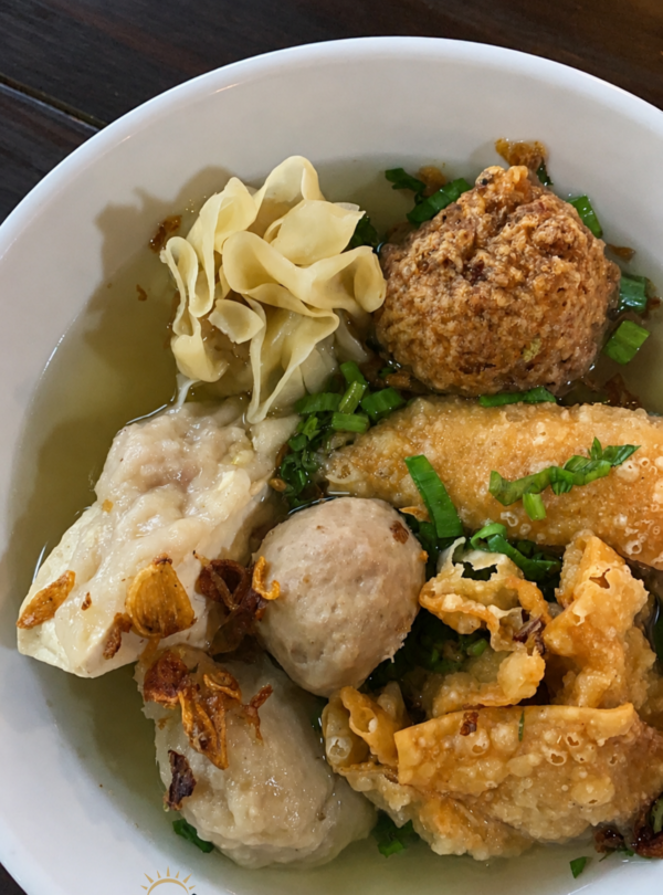 A bowl of Bakso Malang featuring meatballs, fried dumplings, tofu, siomay, crispy wontons, and clear savory broth served at Bakso Malang restaurant in Indonesia.