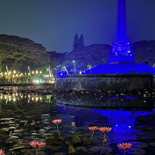 Night view of Balai Kota Malang monument surrounded by a lotus pond with blooming pink water lilies and blue illumination reflecting beautifully on the water in Malang, Indonesia.