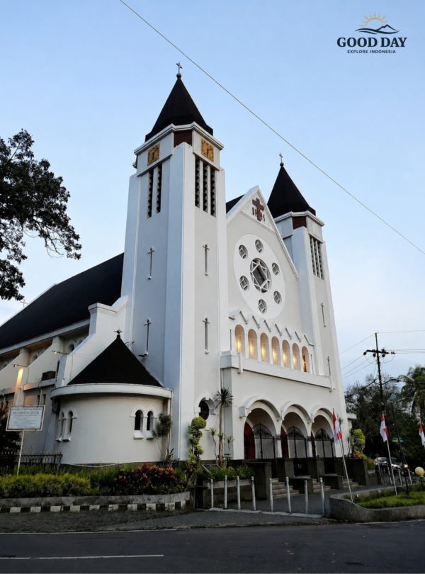 Beautiful white Catholic church with twin towers and black rooftops viewed from the street during sunset in Indonesia, featuring classic European-inspired architecture and peaceful evening atmosphere.