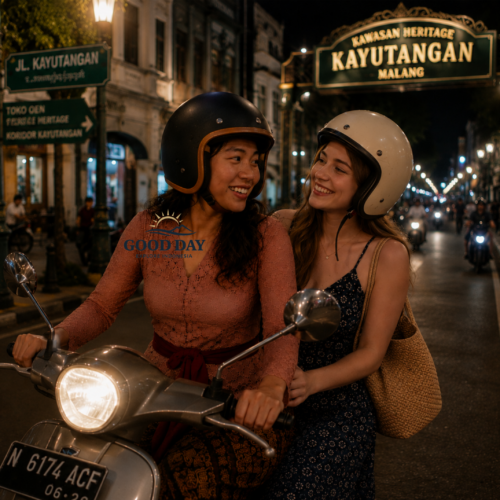 Two women riding a scooter at night in Kayutangan Heritage Malang, Indonesia, wearing helmets and smiling while exploring the vibrant historic street filled with city lights and colonial architecture.