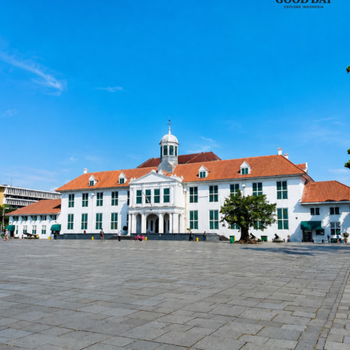 Historic Fatahillah Museum building in Jakarta Old Town featuring Dutch colonial architecture, white facade, red roof tiles, and a large public square under a bright blue sky in Jakarta, Indonesia.