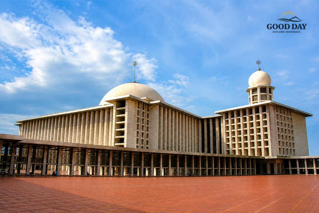 Exterior view of Istiqlal Mosque Jakarta featuring massive modern Islamic architecture, large central dome, spacious courtyard, and iconic prayer hall under a blue cloudy sky in Jakarta, Indonesia.