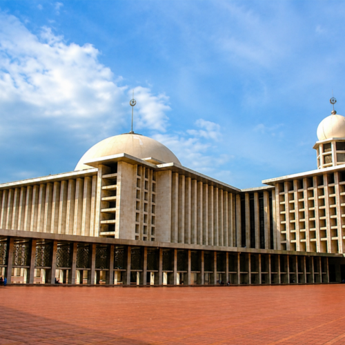 Exterior view of Istiqlal Mosque Jakarta featuring massive modern Islamic architecture, large central dome, spacious courtyard, and iconic prayer hall under a blue cloudy sky in Jakarta, Indonesia.