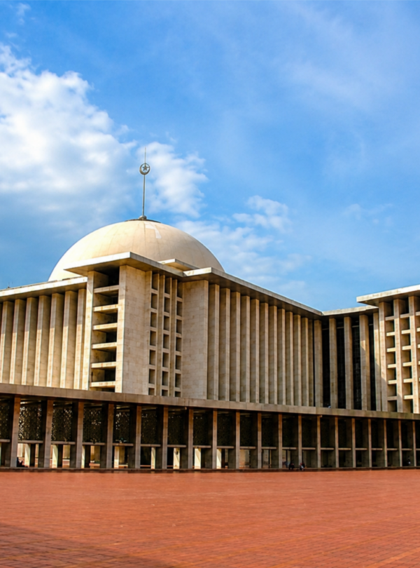Exterior view of Istiqlal Mosque Jakarta featuring massive modern Islamic architecture, large central dome, spacious courtyard, and iconic prayer hall under a blue cloudy sky in Jakarta, Indonesia.