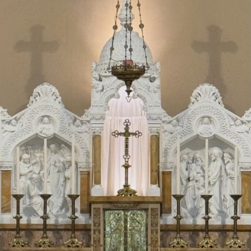 Sacred altar inside Jakarta Catholic Cathedral featuring ornate white Gothic carvings, Christian sculptures, candles, a hanging sanctuary lamp, and a central cross beneath stained glass windows in Jakarta, Indonesia.