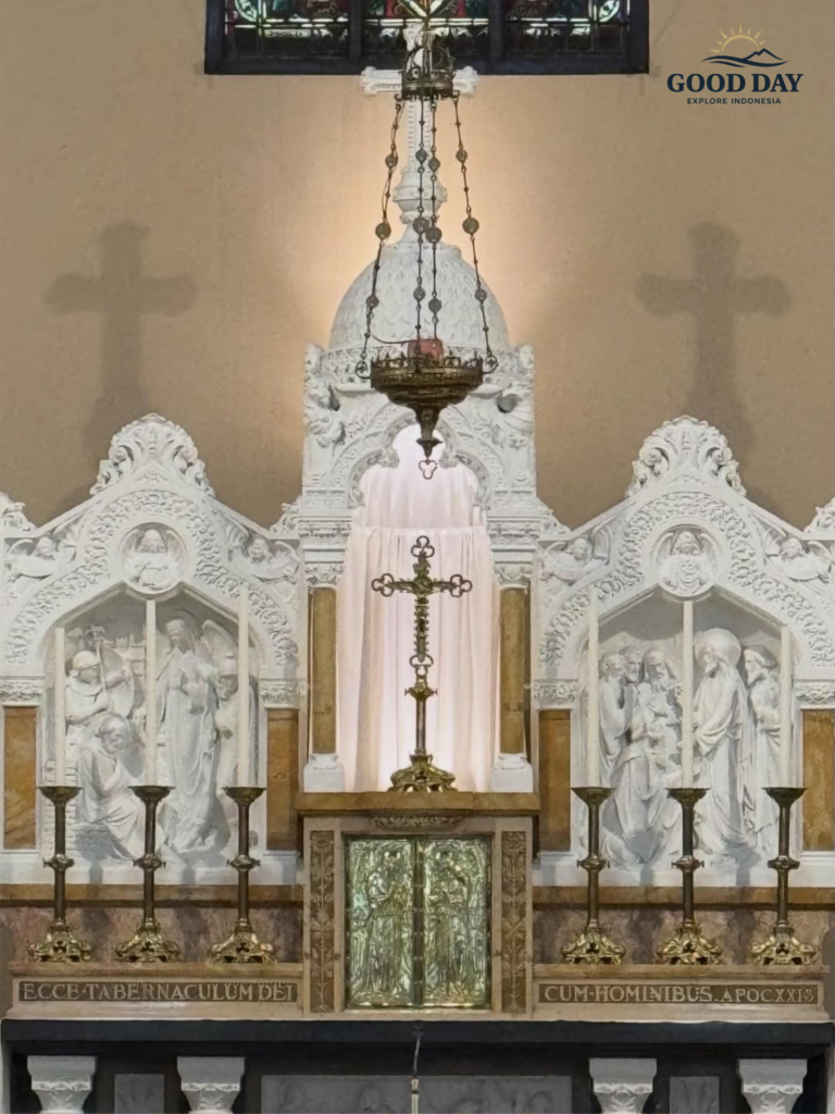 Sacred altar inside Jakarta Catholic Cathedral featuring ornate white Gothic carvings, Christian sculptures, candles, a hanging sanctuary lamp, and a central cross beneath stained glass windows in Jakarta, Indonesia.