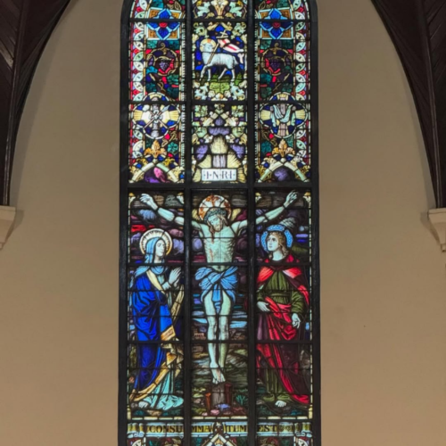 Stained glass window inside the Jakarta Catholic Cathedral featuring the crucifixion of Jesus Christ, with intricate Gothic-style religious artwork, vibrant blue and red colors, and sacred Christian symbolism in Jakarta, Indonesia