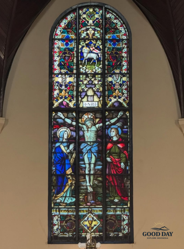 Stained glass window inside the Jakarta Catholic Cathedral featuring the crucifixion of Jesus Christ, with intricate Gothic-style religious artwork, vibrant blue and red colors, and sacred Christian symbolism in Jakarta, Indonesia
