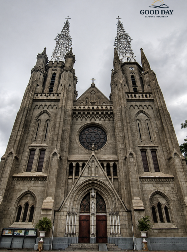 Front exterior view of Jakarta Catholic Cathedral featuring Neo-Gothic architecture, tall twin spires, arched entrances, and historic stone facade under a cloudy sky in Jakarta, Indonesia