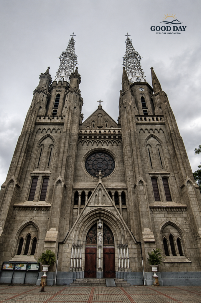 Front exterior view of Jakarta Catholic Cathedral featuring Neo-Gothic architecture, tall twin spires, arched entrances, and historic stone facade under a cloudy sky in Jakarta, Indonesia