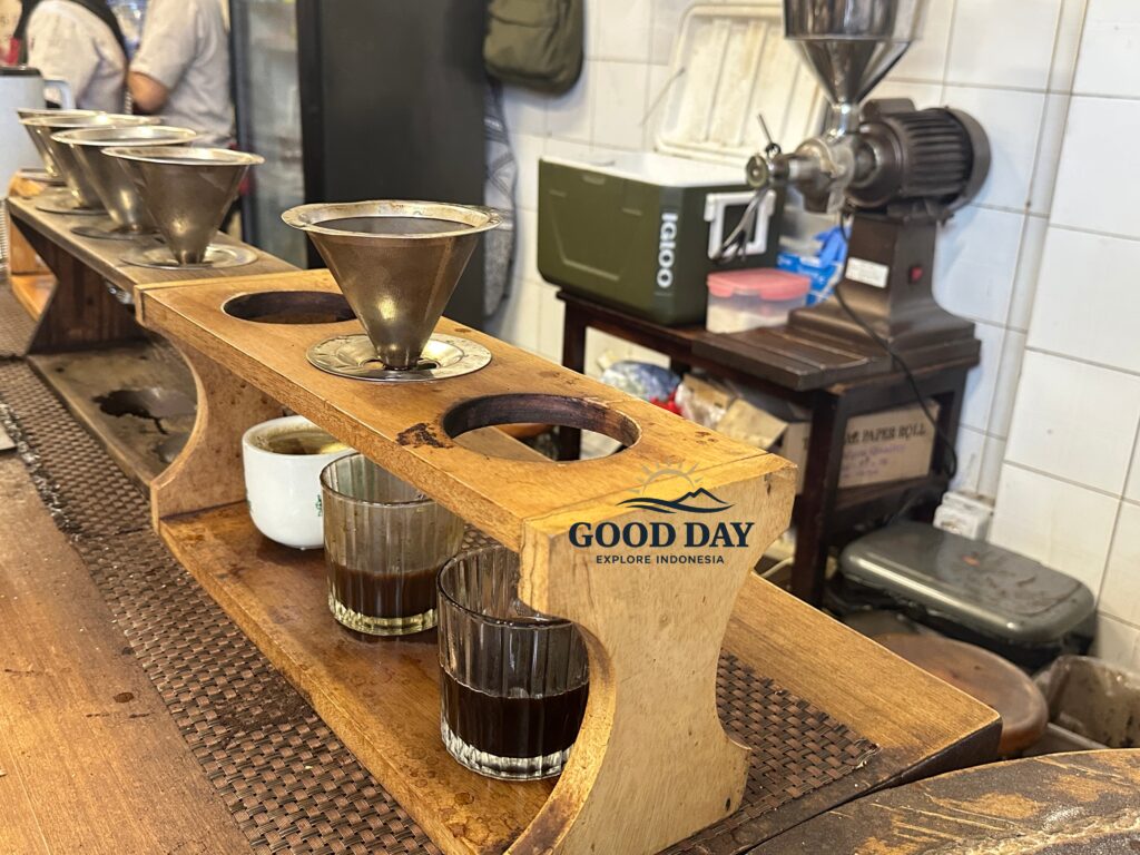 Traditional manual brew coffee setup at a café in Glodok Jakarta featuring metal coffee filters, freshly brewed black coffee, wooden brewing stations, and vintage coffee-making equipment.