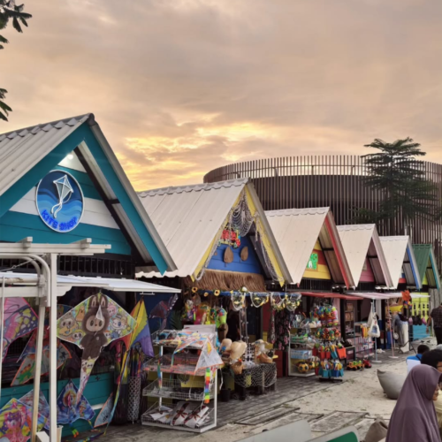 Colorful beachside souvenir shops at Aloha PIK Jakarta during sunset, featuring local merchandise, kites, and a tropical coastal atmosphere in Pantai Indah Kapuk.