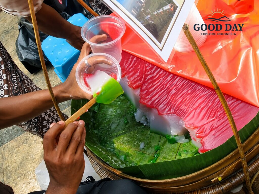 Traditional Selendang Mayang dessert being freshly served by a Jakarta street vendor, featuring colorful rice flour jelly in red, white, and green layers prepared for customers at a local market.