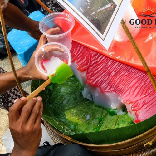 Traditional Selendang Mayang dessert being freshly served by a Jakarta street vendor, featuring colorful rice flour jelly in red, white, and green layers prepared for customers at a local market.