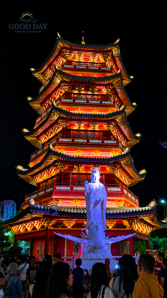 Colorfully illuminated Chinese-style pagoda at PIK 2 Jakarta at night, featuring traditional architecture, vibrant red and gold lighting, a large Buddhist statue, and visitors exploring the cultural attraction.