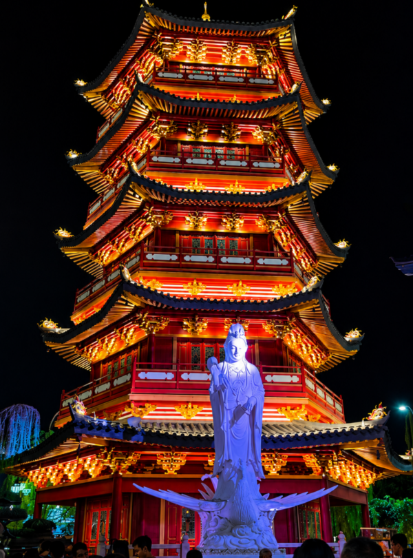 Colorfully illuminated Chinese-style pagoda at PIK 2 Jakarta at night, featuring traditional architecture, vibrant red and gold lighting, a large Buddhist statue, and visitors exploring the cultural attraction.