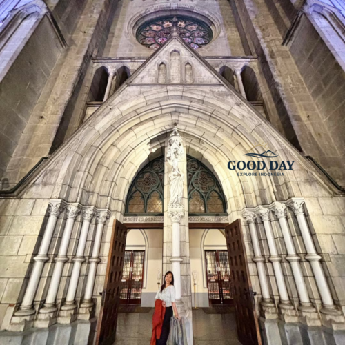 Visitor standing at the grand entrance of Jakarta Cathedral, surrounded by soaring Neo-Gothic arches, intricate stone carvings, and historic architectural details. The magnificent façade showcases one of Jakarta's most iconic religious landmarks and cultural heritage sites.