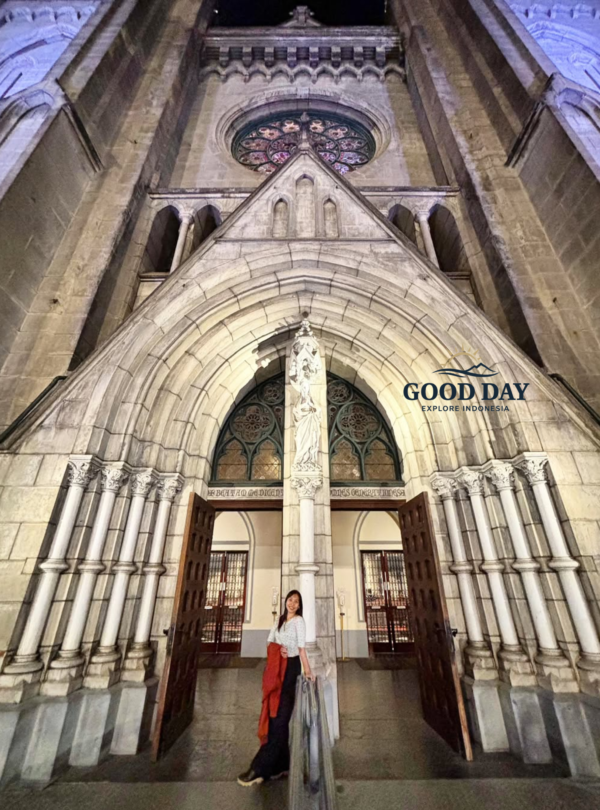 Visitor standing at the grand entrance of Jakarta Cathedral, surrounded by soaring Neo-Gothic arches, intricate stone carvings, and historic architectural details. The magnificent façade showcases one of Jakarta's most iconic religious landmarks and cultural heritage sites.