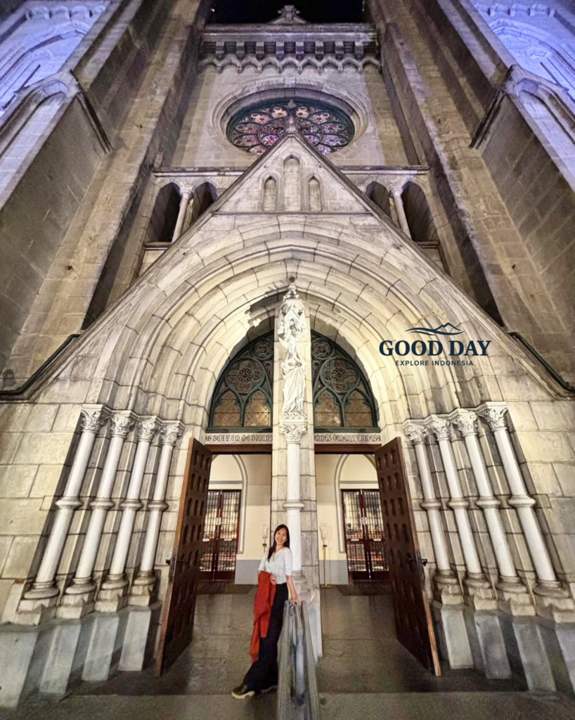 Visitor standing at the grand entrance of Jakarta Cathedral, surrounded by soaring Neo-Gothic arches, intricate stone carvings, and historic architectural details. The magnificent façade showcases one of Jakarta's most iconic religious landmarks and cultural heritage sites.