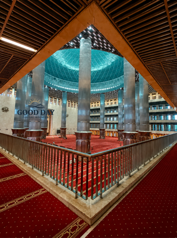 Interior of Istiqlal Mosque Jakarta featuring towering marble columns, a massive central prayer hall, red prayer carpets, and a magnificent domed ceiling. The grand architecture showcases the largest mosque in Southeast Asia and one of Jakarta's most iconic religious landmarks.