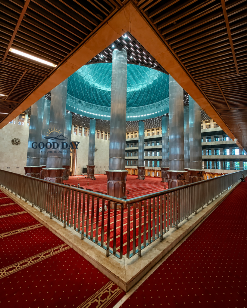 Interior of Istiqlal Mosque Jakarta featuring towering marble columns, a massive central prayer hall, red prayer carpets, and a magnificent domed ceiling. The grand architecture showcases the largest mosque in Southeast Asia and one of Jakarta's most iconic religious landmarks.