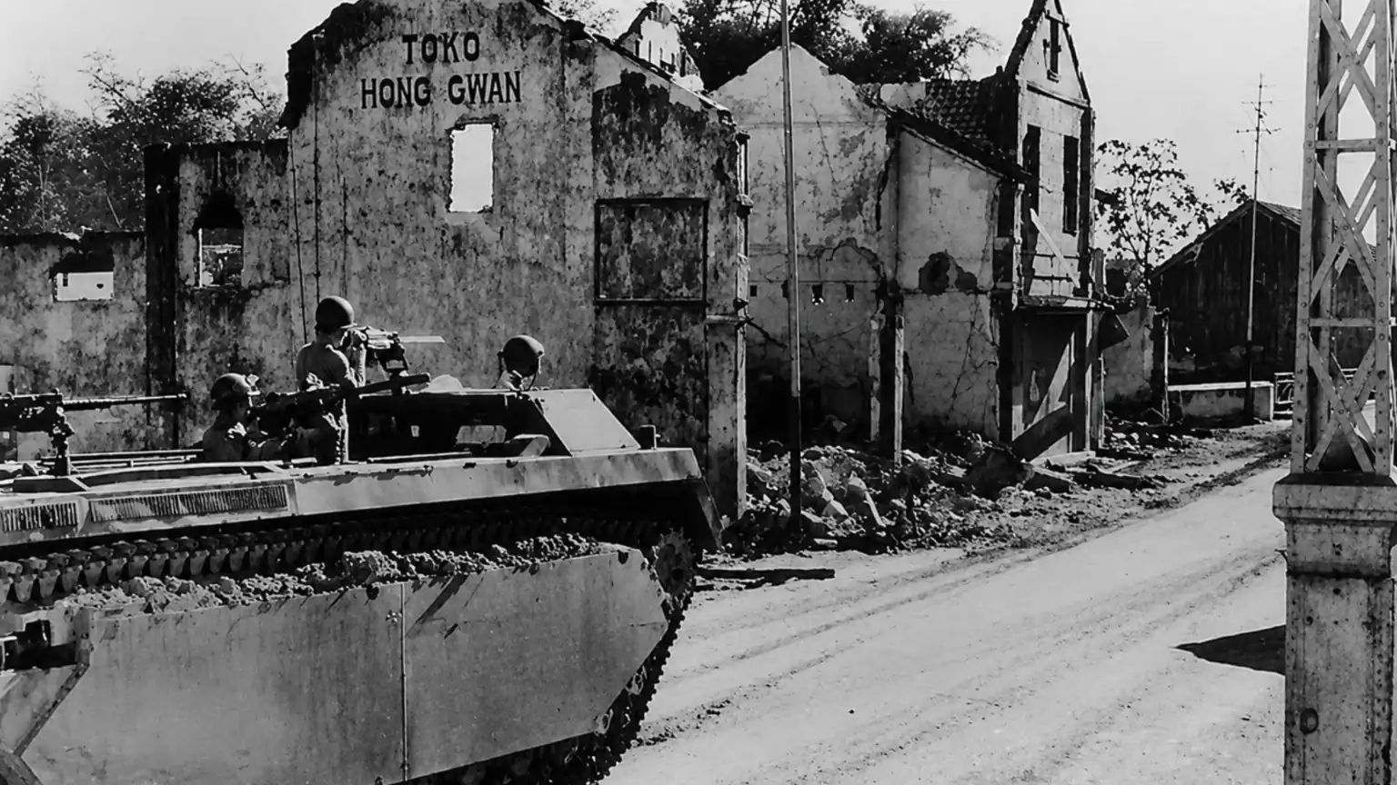 British military armored vehicle advancing past the ruined Hong Gwan building during the Battle of Surabaya in November 1945, one of the largest battles of the Indonesian National Revolution.