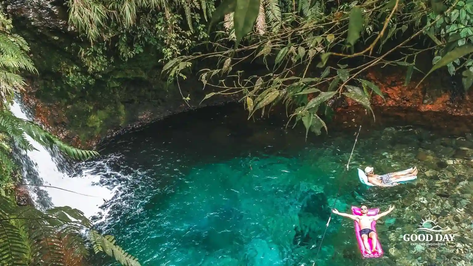 Visitors relaxing in the crystal-clear natural pool at Curug Pangeran Waterfall in Bogor, West Java, Indonesia, surrounded by lush tropical rainforest.