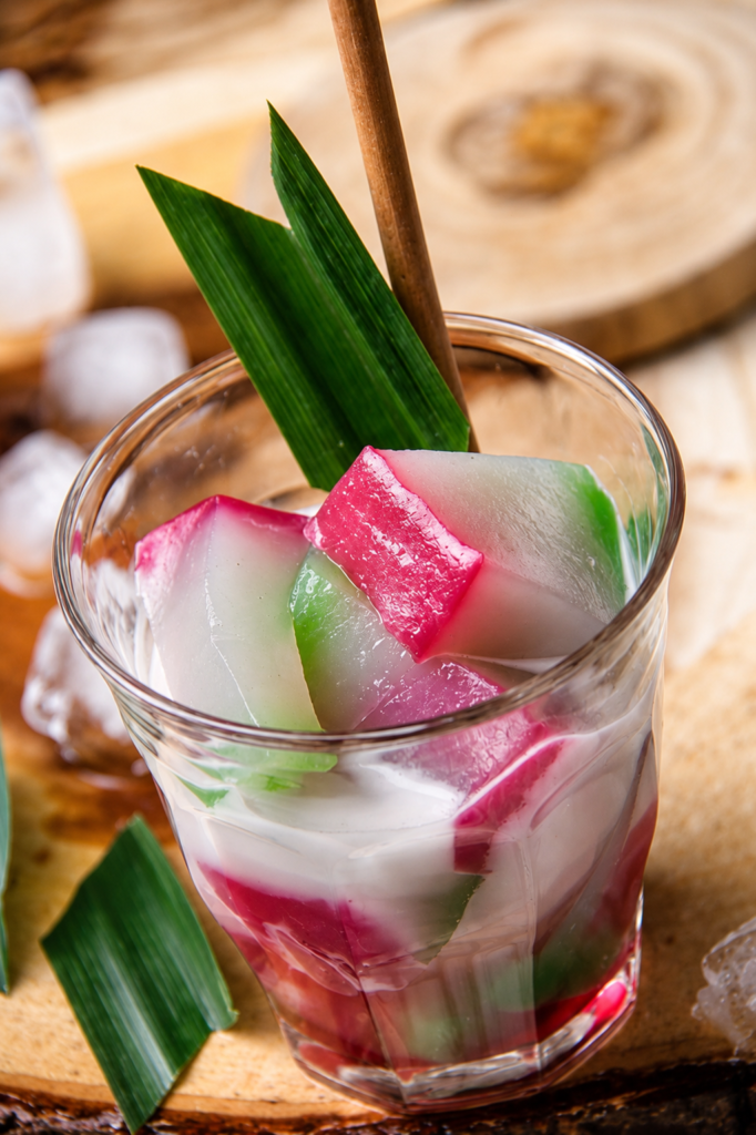 Traditional Selendang Mayang dessert from Jakarta featuring colorful rice flour jelly, creamy coconut milk, and palm sugar syrup served in a glass cup.