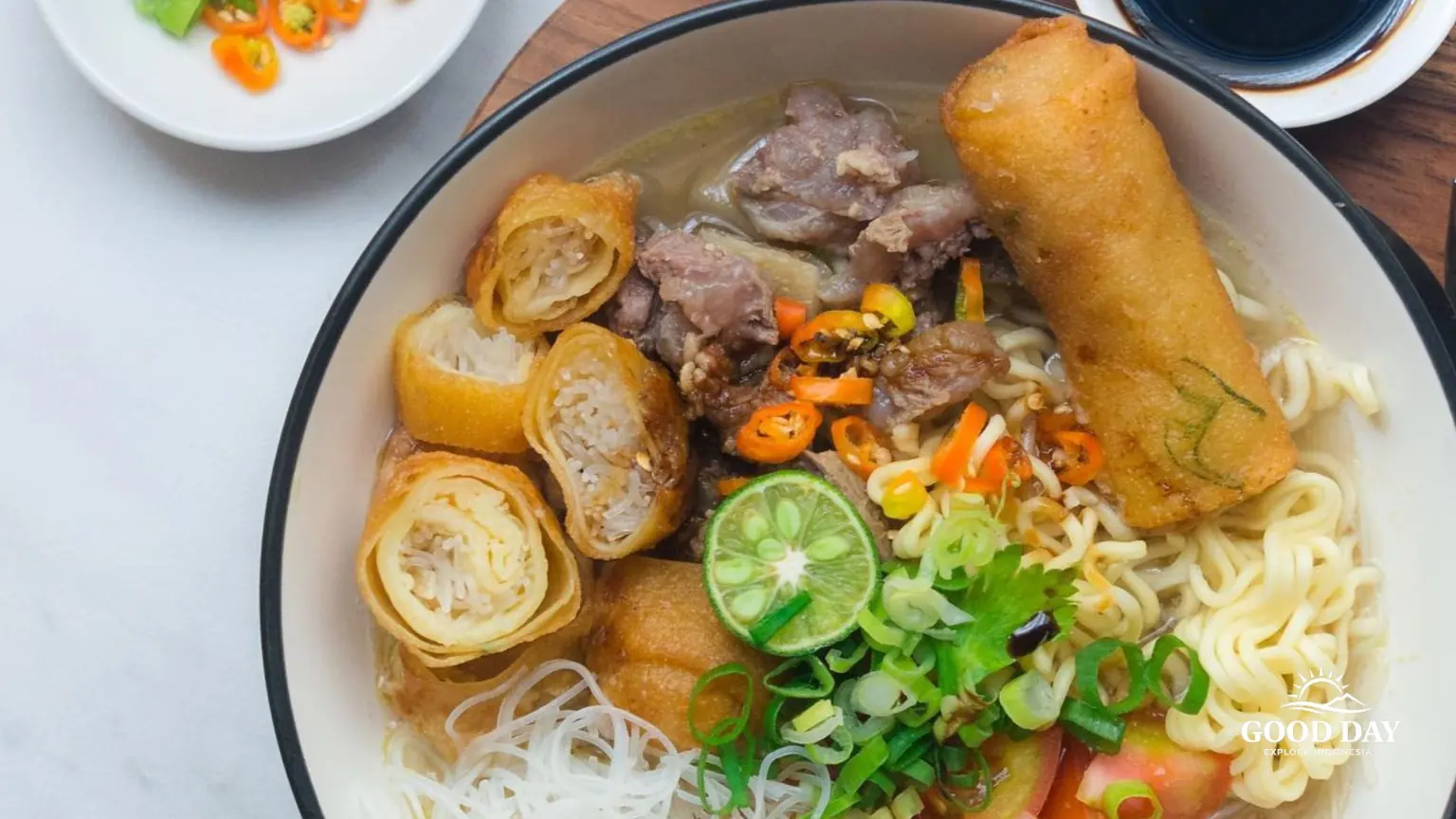 A bowl of Soto Mie Bogor, a traditional Indonesian noodle soup with beef, rice vermicelli, yellow noodles, crispy spring rolls, tomatoes, lime, and savory clear broth in Bogor, West Java.
