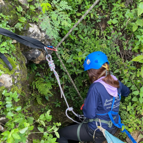 Participant preparing for a vertical caving descent at Goa Macan Mati in Yogyakarta, Indonesia. Equipped with a safety harness, helmet, and professional rope system, the adventurer begins an exciting cave exploration through the lush karst landscape of Gunungkidul, one of Jogja's top destinations for outdoor adventure tourism.