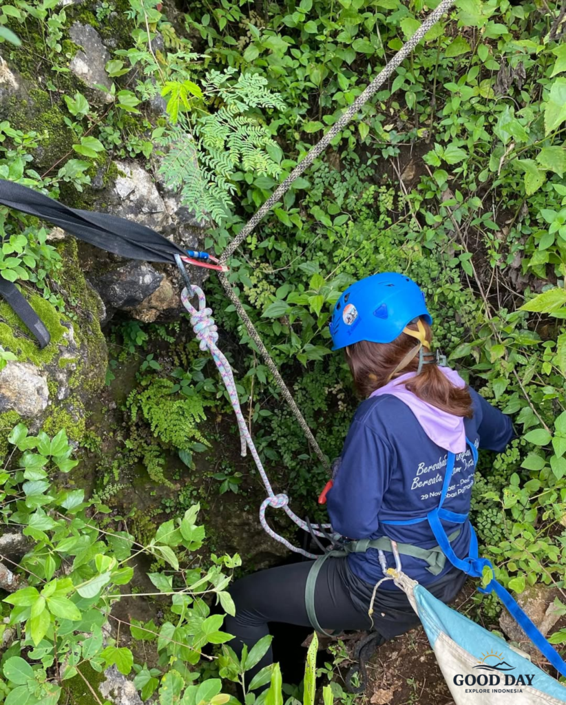 Participant preparing for a vertical caving descent at Goa Macan Mati in Yogyakarta, Indonesia. Equipped with a safety harness, helmet, and professional rope system, the adventurer begins an exciting cave exploration through the lush karst landscape of Gunungkidul, one of Jogja's top destinations for outdoor adventure tourism.