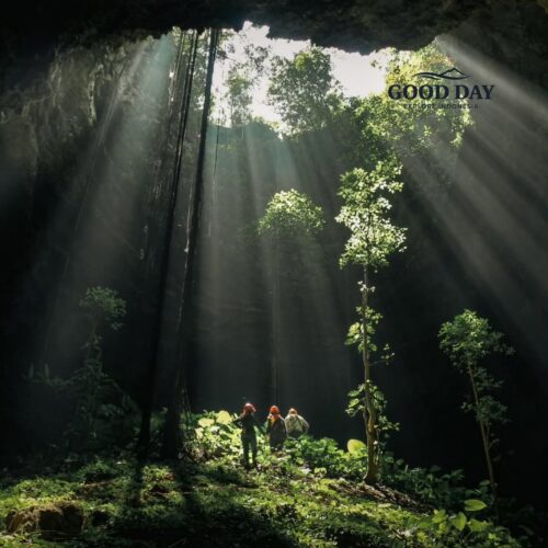 Sunlight streams dramatically through the massive opening of Goa Macan Mati in Yogyakarta, Indonesia, illuminating lush vegetation and cave explorers deep inside the underground chamber. This breathtaking cave landscape showcases one of Gunungkidul's most spectacular natural wonders, where adventure, geology, and nature converge beneath the Earth's surface.