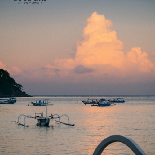 Traditional outrigger boats floating on calm waters during sunset in Lombok, Indonesia, with soft pastel clouds reflecting on the sea and creating a peaceful tropical coastal scene.