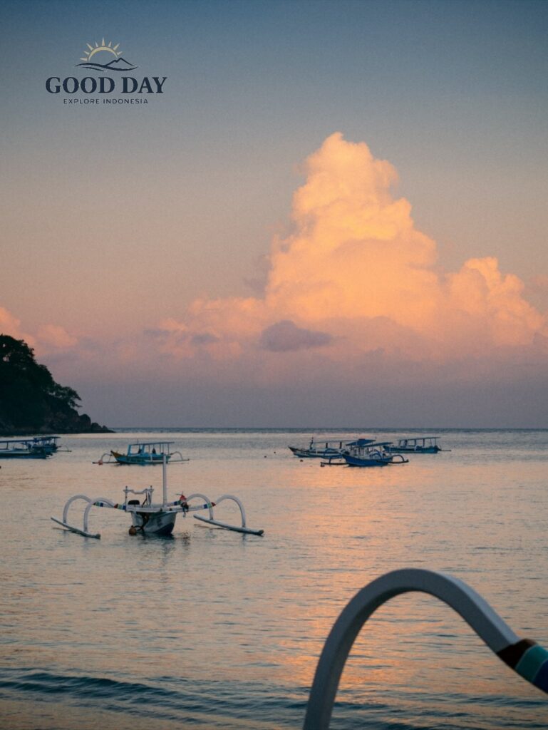 Traditional outrigger boats floating on calm waters during sunset in Lombok, Indonesia, with soft pastel clouds reflecting on the sea and creating a peaceful tropical coastal scene.