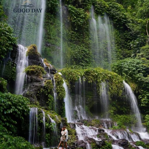 Benang Kelambu Waterfall in Lombok, Indonesia, cascading down lush green cliffs covered in tropical vegetation, with visitors standing below to admire one of the island’s most beautiful natural attractions.