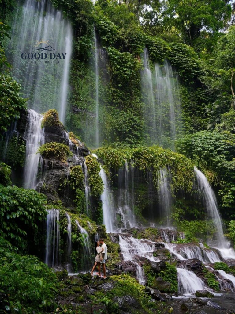 Benang Kelambu Waterfall in Lombok, Indonesia, cascading down lush green cliffs covered in tropical vegetation, with visitors standing below to admire one of the island’s most beautiful natural attractions.