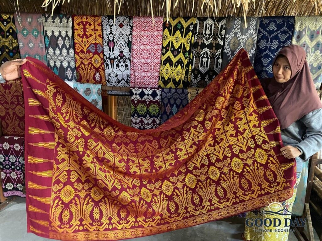 Traditional Sasak woven textile (Songket Lombok) displayed by a local artisan in Sade Traditional Village, Lombok. The handcrafted red and gold fabric features intricate geometric patterns and cultural motifs, showcasing the rich weaving heritage of the Sasak people.