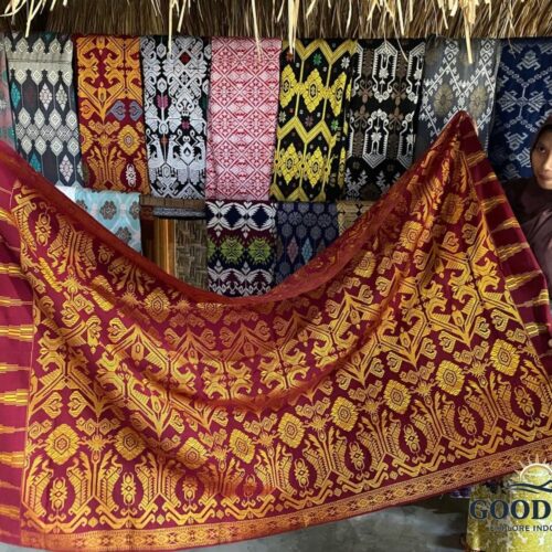 Traditional Sasak woven textile (Songket Lombok) displayed by a local artisan in Sade Traditional Village, Lombok. The handcrafted red and gold fabric features intricate geometric patterns and cultural motifs, showcasing the rich weaving heritage of the Sasak people.