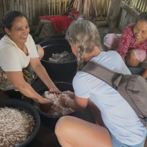 Traveler learning how to make traditional coconut oil with local villagers in Lombok, Indonesia. The hands-on cultural experience showcases the traditional process of extracting coconut oil using fresh grated coconut in a rural village setting.