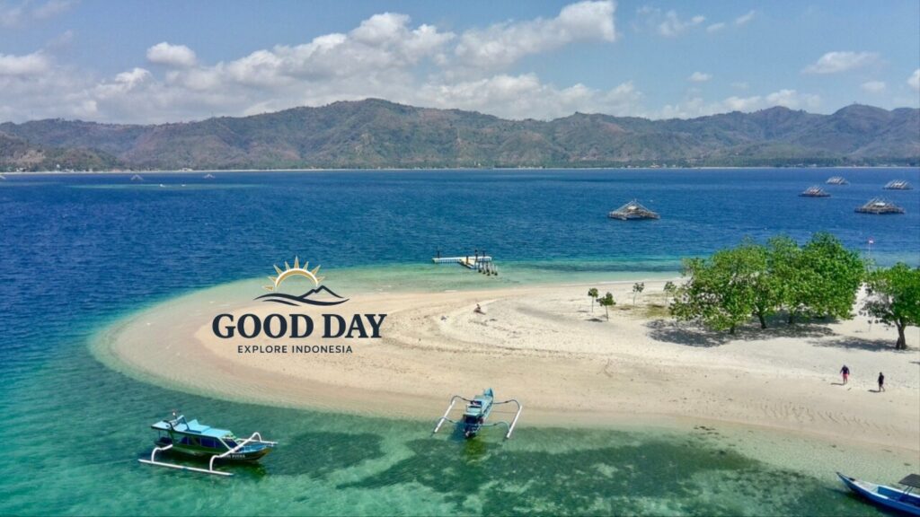 Aerial view of a pristine Gili island in Lombok featuring a white sandbar, crystal-clear turquoise waters, traditional Indonesian outrigger boats, and a tropical shoreline surrounded by the stunning coastline of Lombok.