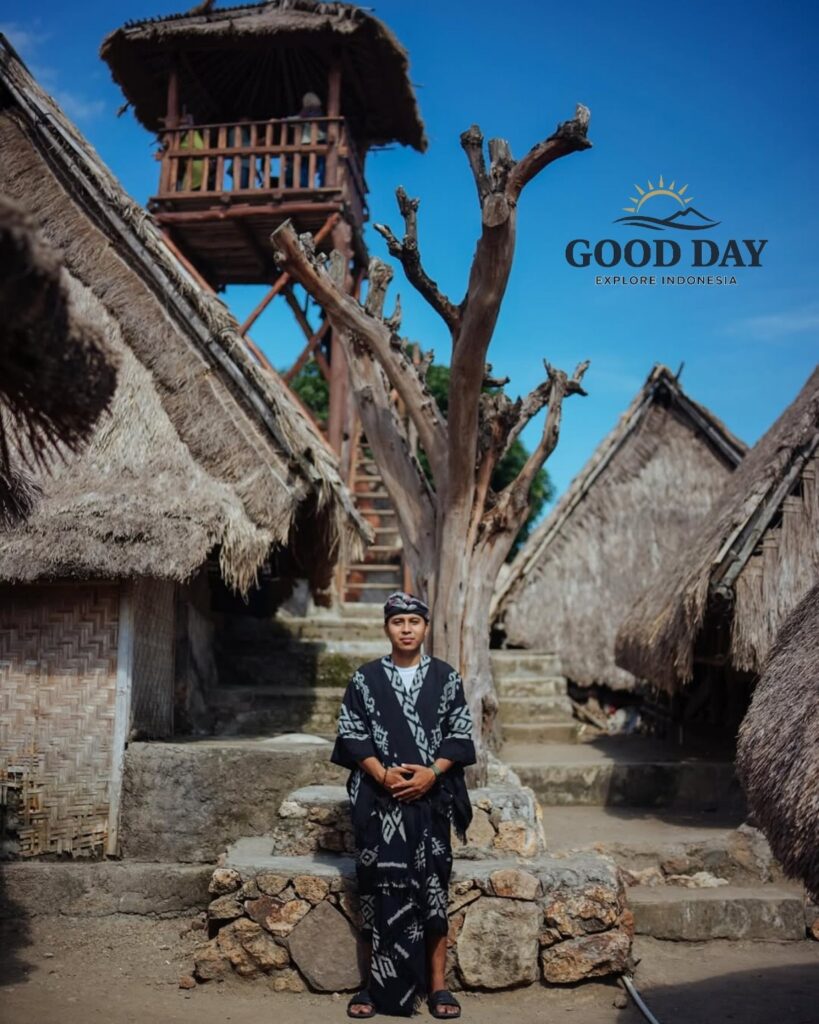 Traditional Sasak villager wearing customary clothing standing among authentic thatched-roof houses at Sade Traditional Village in Lombok, Indonesia, showcasing the rich cultural heritage and traditional architecture of the Sasak people.