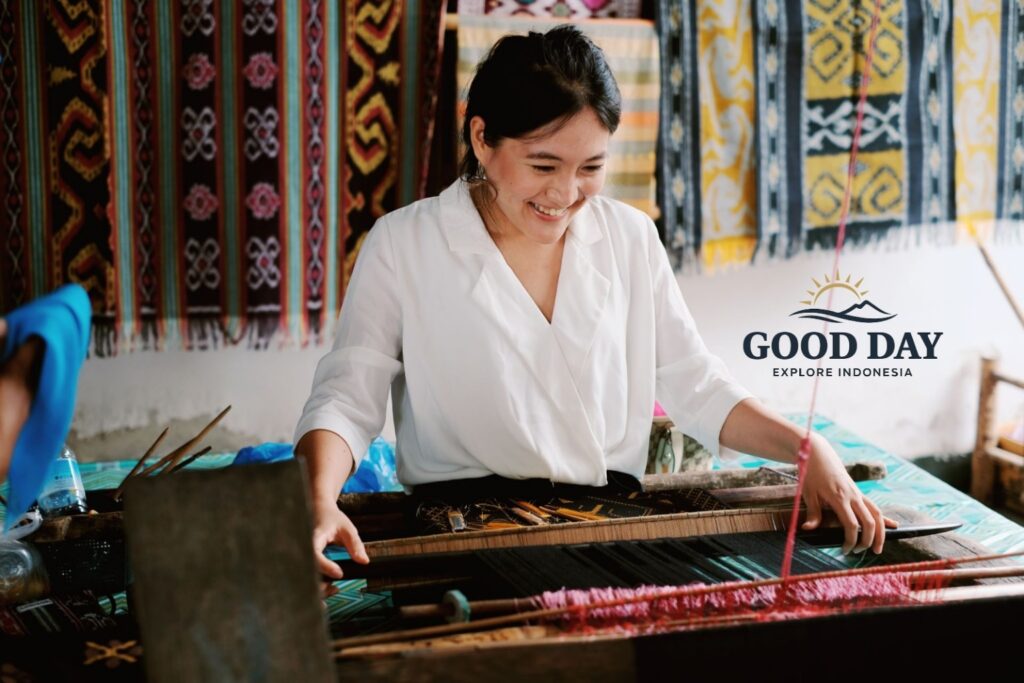 Visitor learning traditional Sasak hand-weaving techniques at Sade Traditional Village in Lombok, Indonesia, using a wooden loom surrounded by colorful handwoven textiles and authentic local craftsmanship.