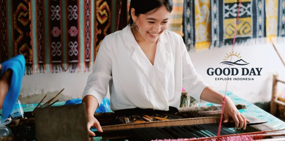Visitor learning traditional Sasak hand-weaving techniques at Sade Traditional Village in Lombok, Indonesia, using a wooden loom surrounded by colorful handwoven textiles and authentic local craftsmanship.