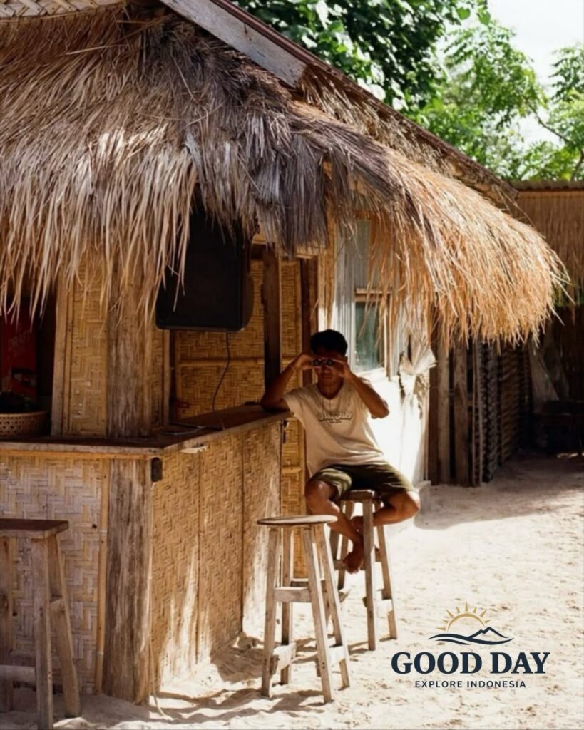 Traditional beachside bamboo hut at Tanjung Aan Beach, Lombok, Indonesia, with a local resident relaxing under a thatched roof surrounded by white sand and tropical island atmosphere.