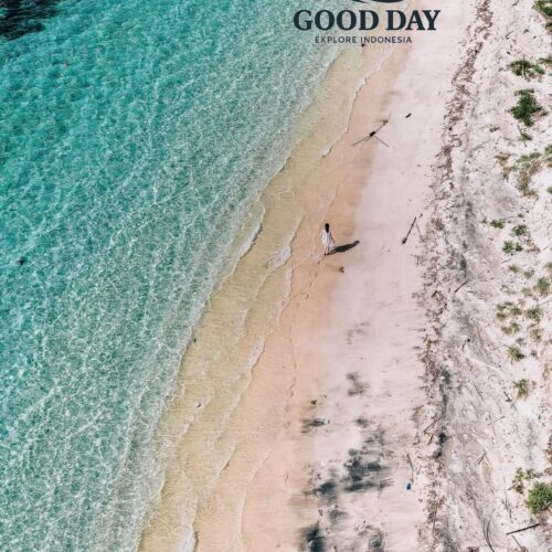 Aerial drone view of a secluded white-sand beach on a Gili Island in Lombok, featuring crystal-clear turquoise water, gentle waves, and a lone traveler walking along the pristine tropical shoreline.