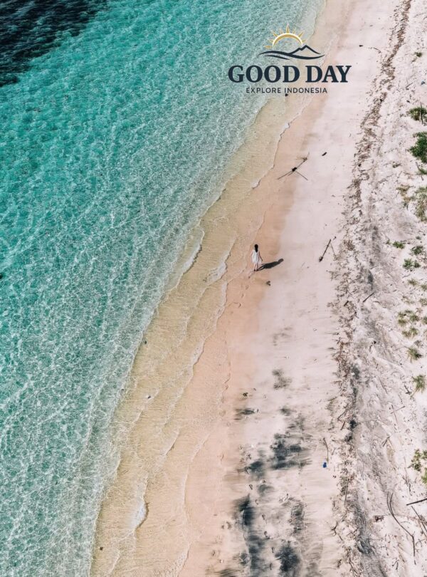 Aerial drone view of a secluded white-sand beach on a Gili Island in Lombok, featuring crystal-clear turquoise water, gentle waves, and a lone traveler walking along the pristine tropical shoreline.
