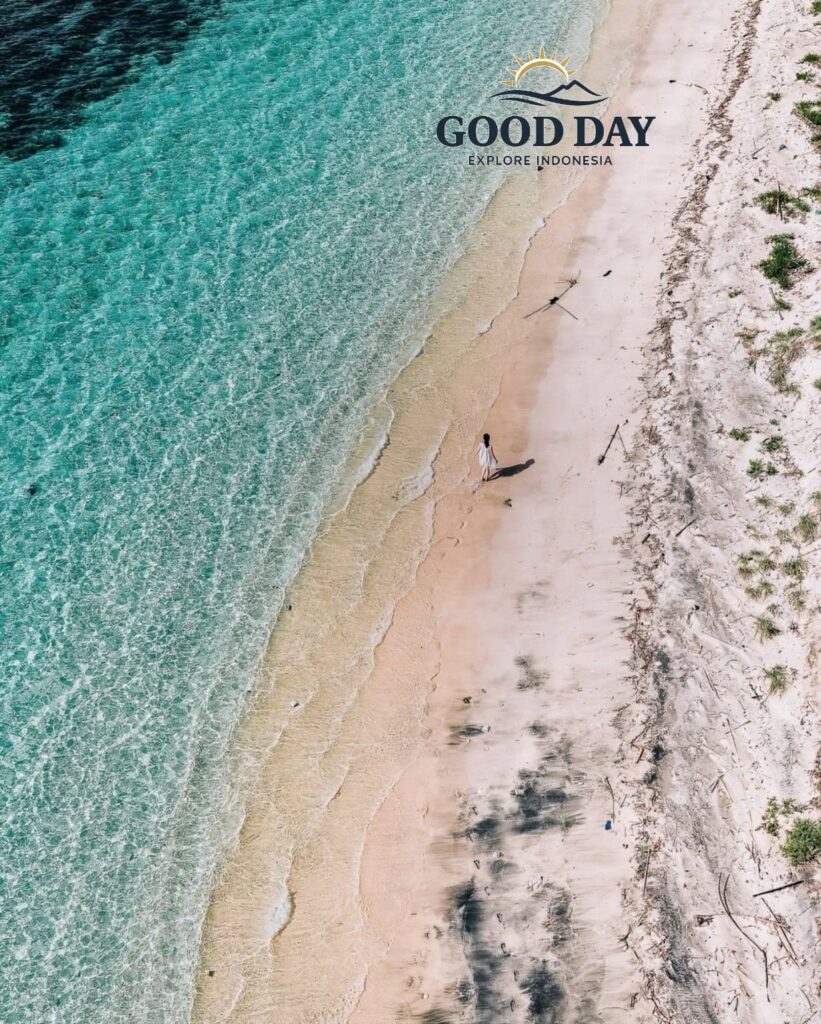 Aerial drone view of a secluded white-sand beach on a Gili Island in Lombok, featuring crystal-clear turquoise water, gentle waves, and a lone traveler walking along the pristine tropical shoreline.